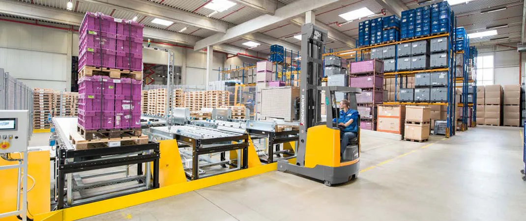 Mann bedient einen Schubmaststapler vor einer Förderanlage