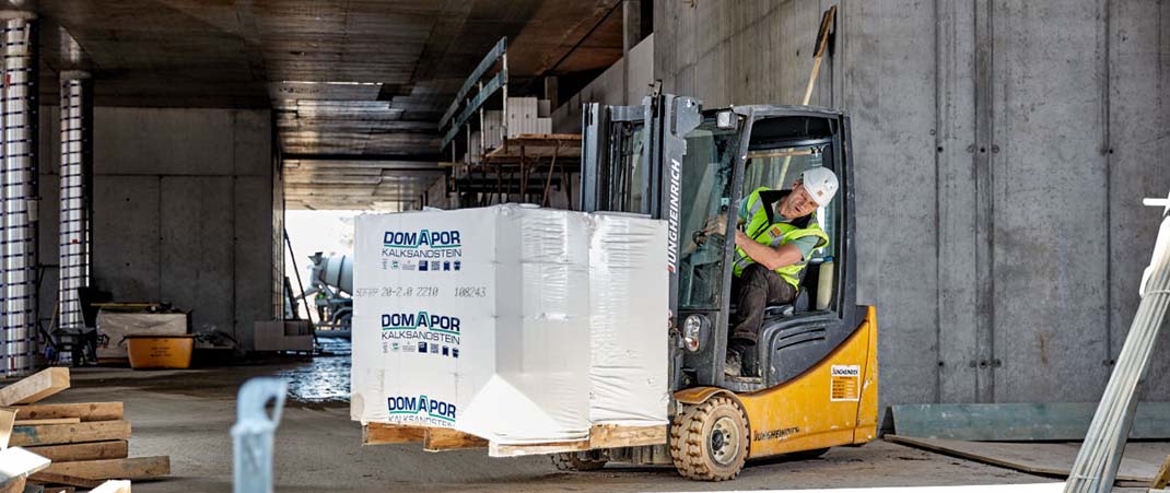 Mann fährt einen  mit Baustoff beladenen Gabelstapler auf einer Baustelle